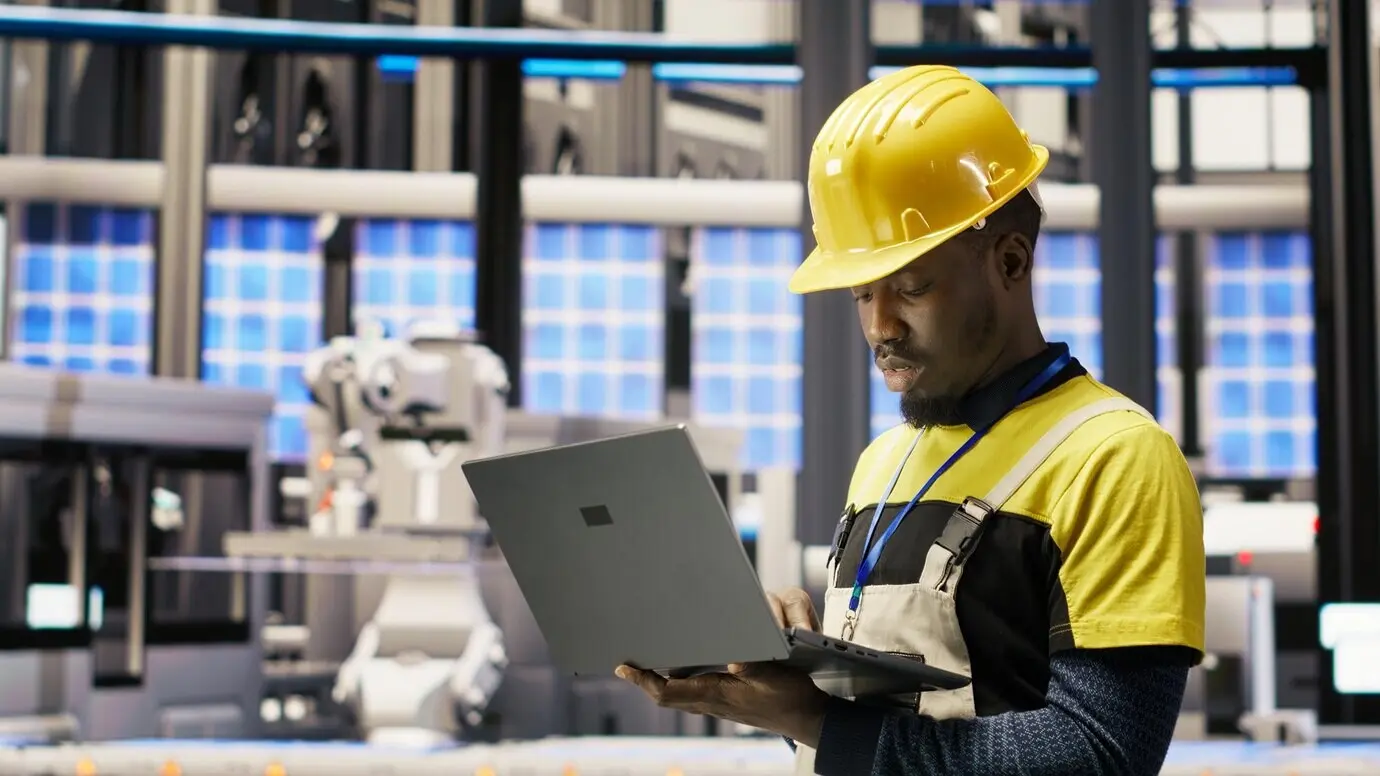 Techniker in einer Solarmodulfabrik überwacht per Laptop die Roboter-Montagelinien.